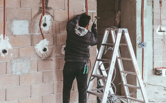 Electricista fijando tubo corrugado en la pared de una vivienda en obra, con las cajas de mecanismos abiertas y los conductores a la vista