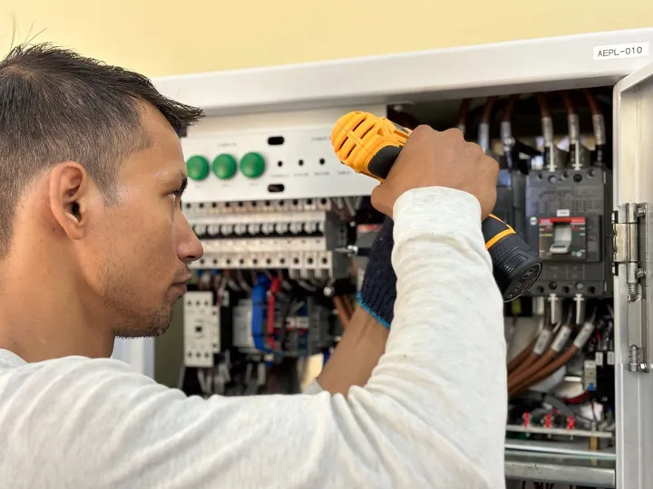 Electricista atornillando en el interior de un cuadro eléctrico, con los magnetotérmicos, los contactores y el embarrado a la vista