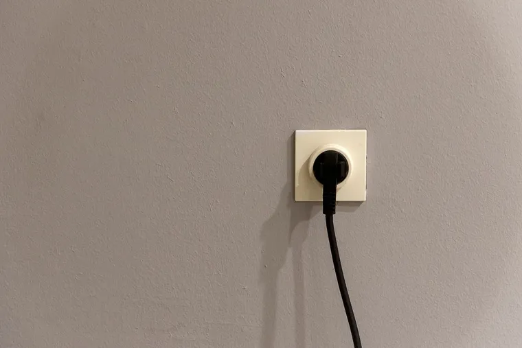 Enchufe de pared de una vivienda con una clavija negra conectada y el cable colgando
