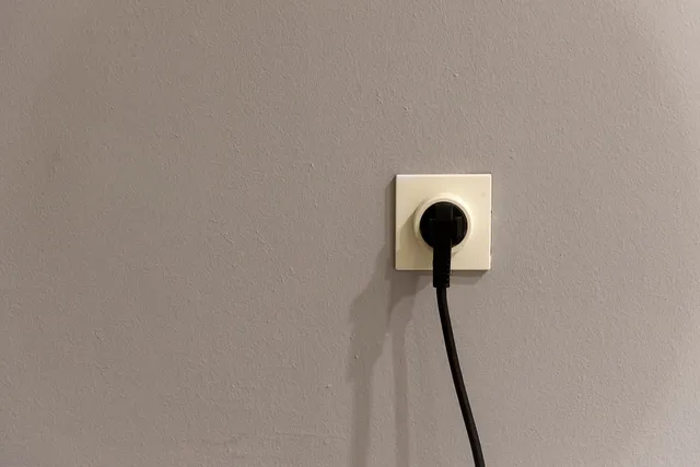 Enchufe de pared de una vivienda con una clavija negra conectada y el cable colgando