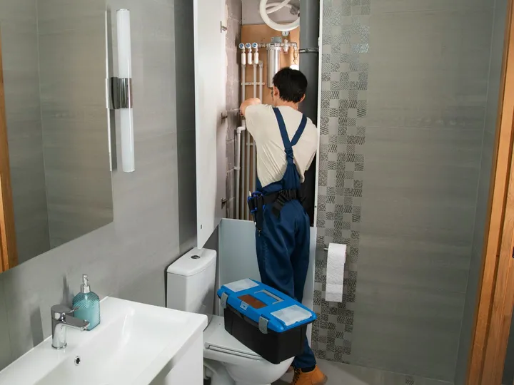 Fontanero trabajando en el registro abierto de la instalación de agua de un baño, con las tuberías, las llaves y las conexiones a la vista