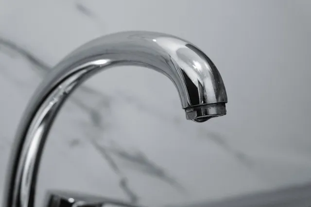 Grifo monomando cromado de un lavabo visto de cerca, con la pared de mármol al fondo