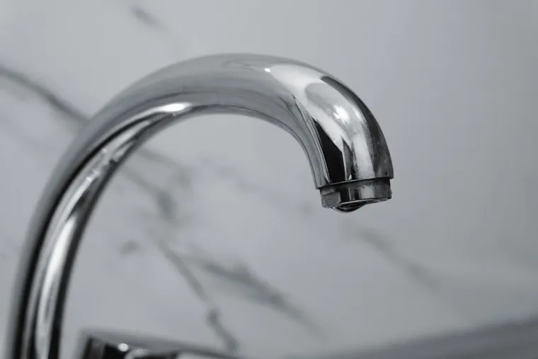 Grifo monomando cromado de un lavabo visto de cerca, con la pared de mármol al fondo