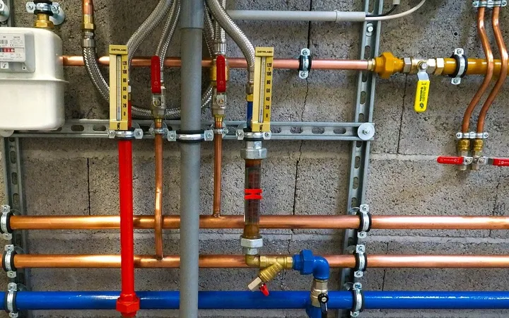 Instalación de fontanería sobre una pared: montantes de cobre de agua fría y caliente, tubos aislados en rojo y azul, llaves de corte y bajante de desagüe