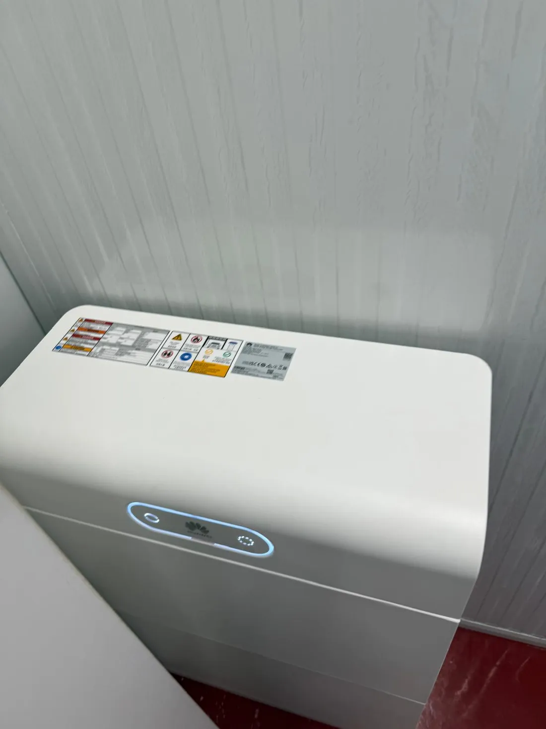 Batería de almacenamiento Huawei con el piloto de estado encendido, instalada junto a la pared del cuarto técnico