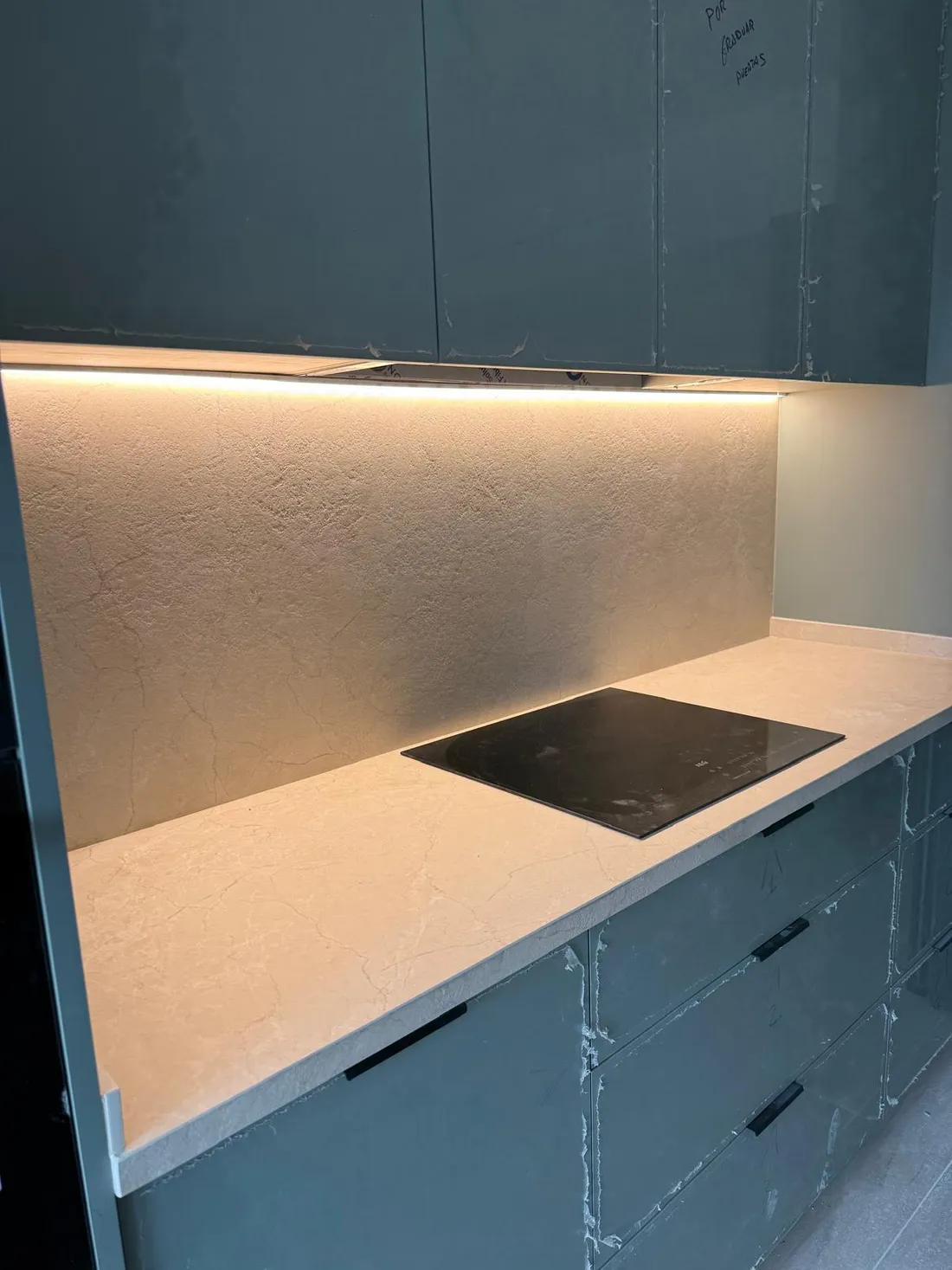 Tira LED bajo los muebles altos iluminando el frente y la encimera junto a la placa de inducción