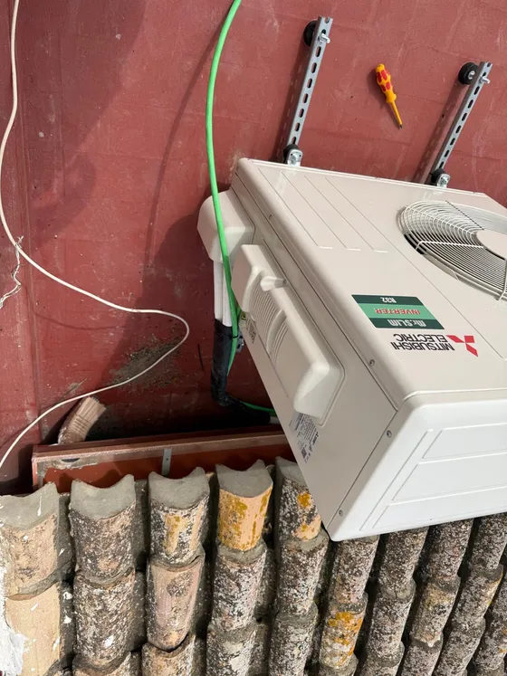 Unidad exterior Mitsubishi Electric fijada sobre perfilería y silentblocks junto a un tejado de teja