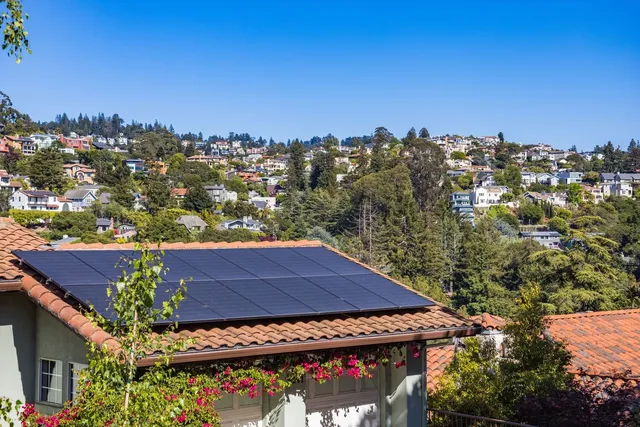 Paneles solares instalados sobre el tejado de teja de una vivienda, con el resto del barrio al fondo