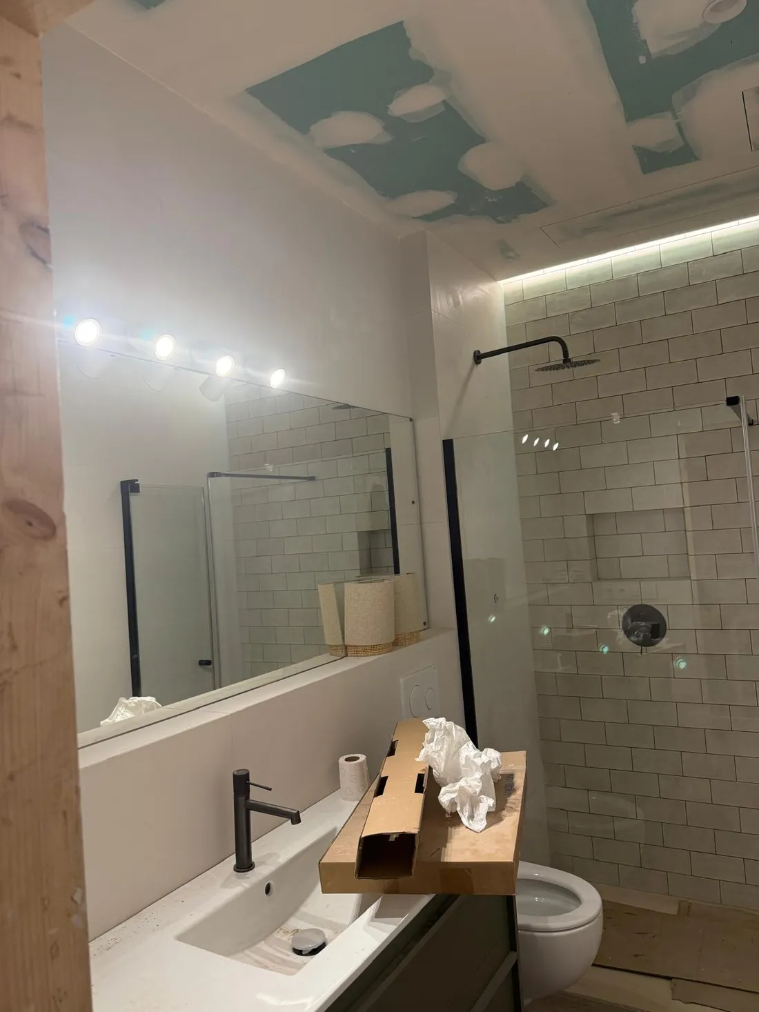 El mismo baño hacia la ducha, con el foco lineal sobre el espejo y la luz indirecta del falso techo encendidas