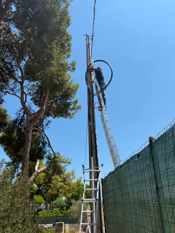 Operario sobre una escalera tendiendo el nuevo cable de acometida en lo alto de un poste de hormigón