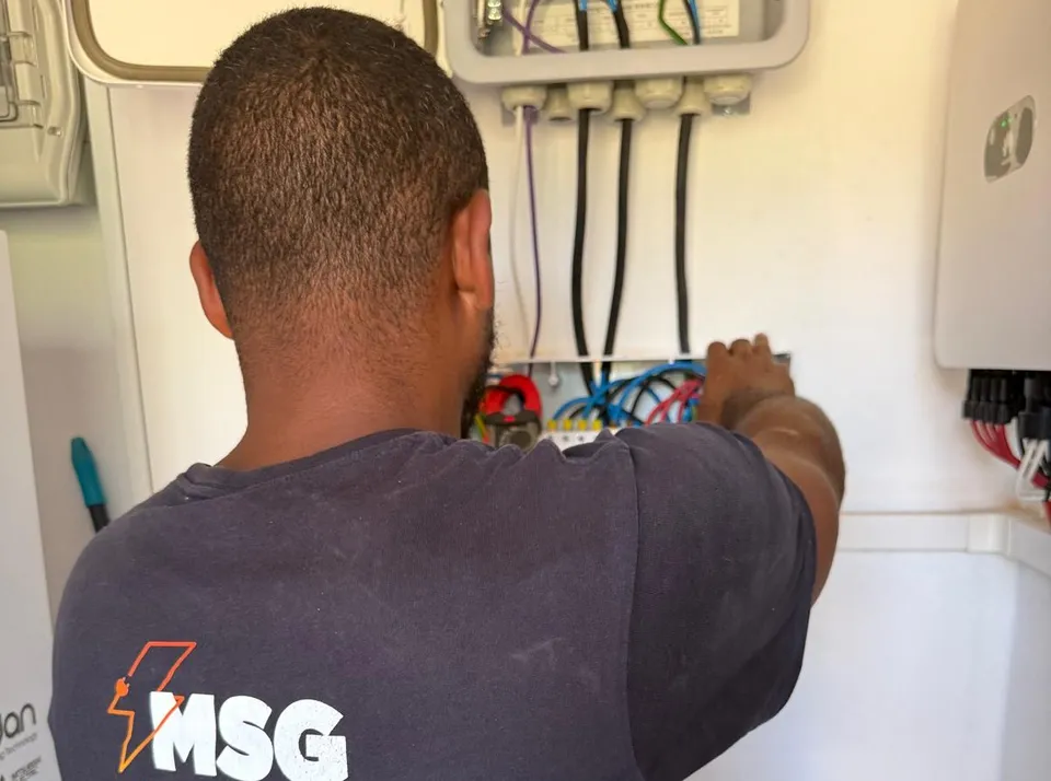 Técnico de MSG con la camiseta de la empresa trabajando en un cuadro eléctrico junto al inversor